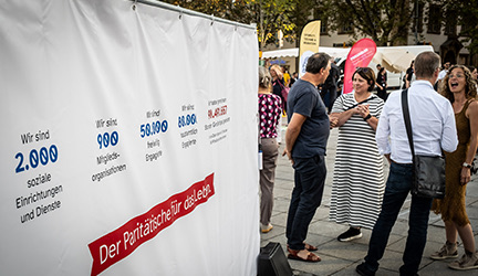 Foto - Menschen vor einem Banner mit wichtigen Zahlen des Paritätischen